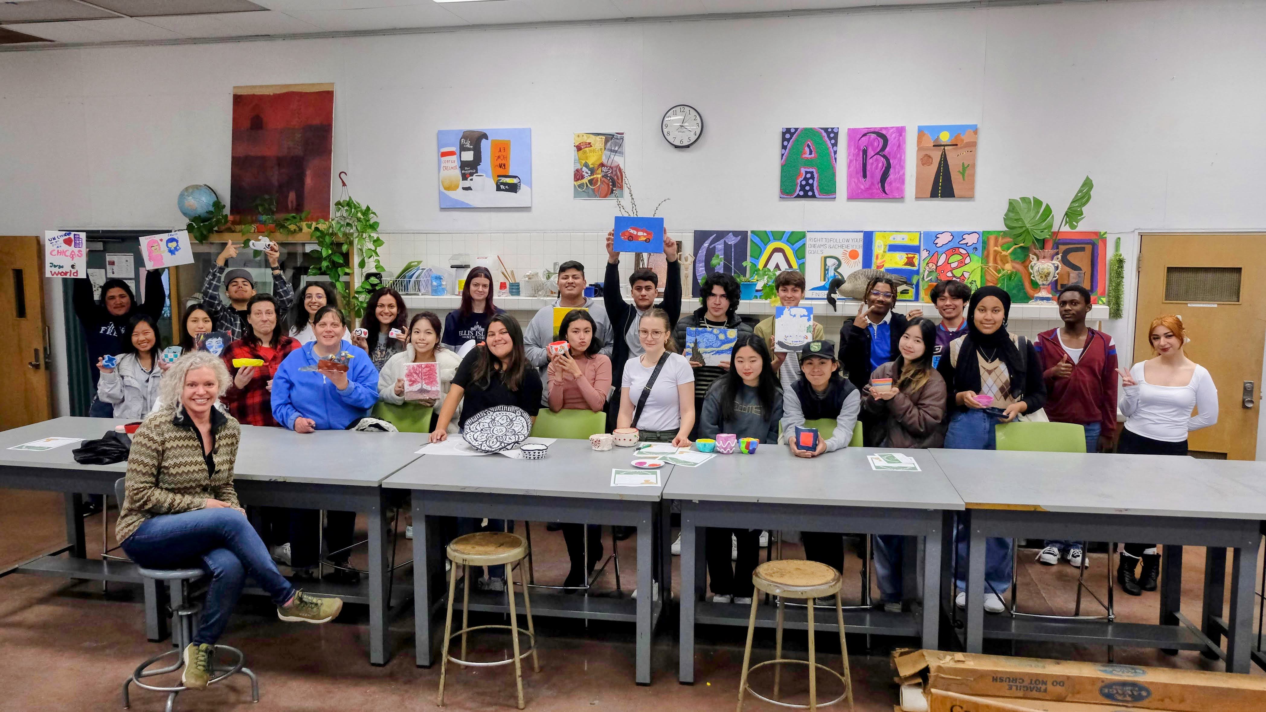 group of students in an art studio showing their art pieces